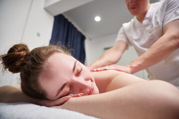 Fototapeta na wymiar Body massage procedure. A woman in a spa salon. The masseur is working on her back