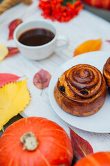 bun, pastry on tray with drink and autumn decoration: fallen yellow leaves and pumpkins. autumn mood