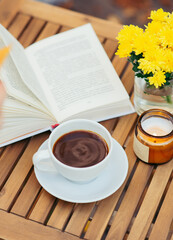yellow flowers, cup of hot drink and book on wooden table outdoor. Autumn still life