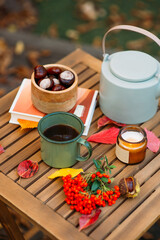 a cup of tea or coffee and a book on a wooden table against the background of fallen leaves, autumn season, still life with leaves, a book and viburnum and chestnuts in the garden outdoors.