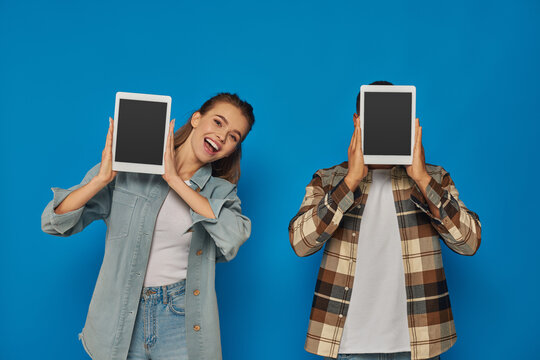 african american man obscuring face with digital tablet near excited woman on blue backdrop