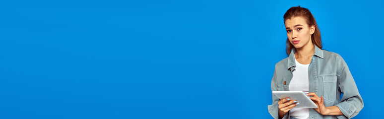 confused young woman holding digital tablet and looking at camera on blue background, banner