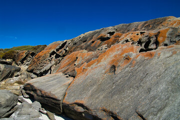 Eroded rocks, covered with orange-brown lichen, at the remote coast of Hamersley Beach in...