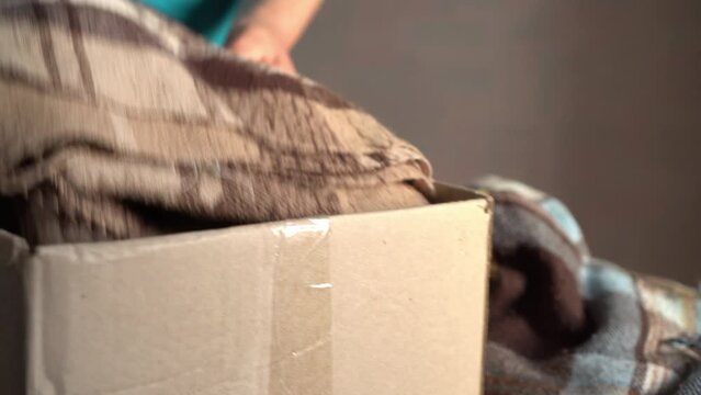  Volunteer stacking warm plaid blankets in a donation box. Woman donates her clothes. Donation. Woman folds clothes, close up. Moving to a new house, putting things in boxes