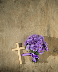 Wooden christian cross with violet Michaelmas daisies flowers on abstract wooden background. Symbol...