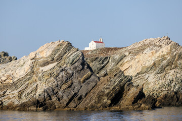 Fototapeta premium Mykonos, Greece - July 21, 2023: A clifftop cross and church on an island off the shores of Mykonos Town in Greece 