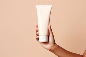 woman hand is holding a white mockup tube of facial cream on a beige isolated background