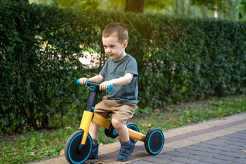 A cute toddler boy of two or three years old rides a bicycle or balance bike in a city park on a...