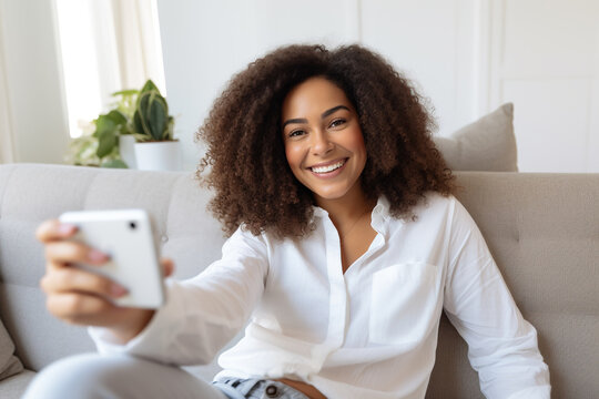 Happy afro American woman relaxing on the sofa at home. Girl taking selfie picture with smartphone