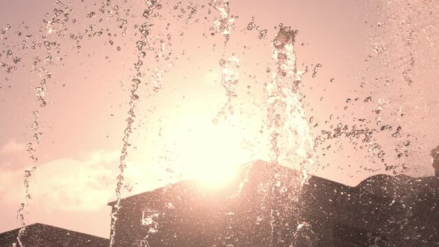 Splashes of fountain close-up on sunny day in sunshine. Slow movement of water droplets of fountain. City park, heat and rising temperatures in summer.