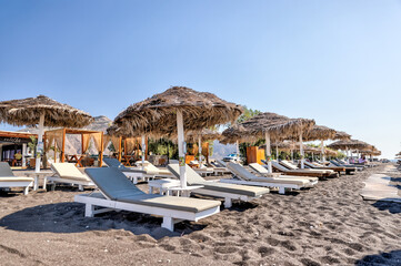 Fira, Greece - July 20, 2023: Palapas and beach chairs on the island of Santorini in Greece
 - obrazy, fototapety, plakaty