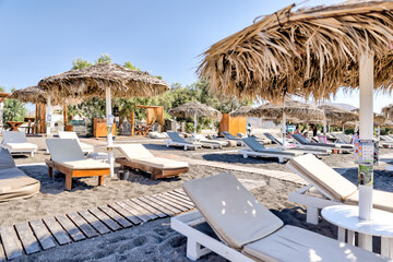 Fira, Greece - July 20, 2023: Palapas and beach chairs on the island of Santorini in Greece
 - obrazy, fototapety, plakaty