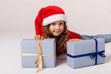 Cute little girl in Santa Claus hat lying down with gifts. White background. Happy New Year and Christmas concept