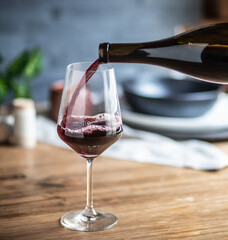 Pouring red wine into a stemmed wine glass on a dinner table