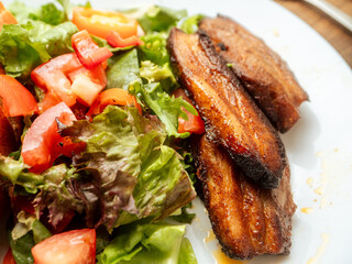 Fresh salad and cooked marinated pork belly slices on white plate. Dinner with tasty pork meat.