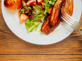 Fresh salad and cooked marinated pork belly slices on white plate. Dinner with tasty pork meat.
