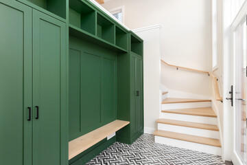 A large foyer with a vibrant green storage unit, white oak bench and stairs, and a black and white...