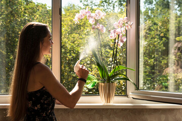 Woman waters the orchids flower in front of the opened window
