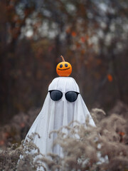 Halloween ghost costume with sunglasses. Cheerful pumpkin on the head. Ghost bed sheet