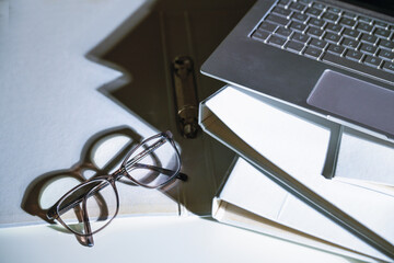 Glasses and a part of a laptop on white file folders with harsh shadows on an office desk, business...