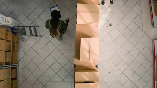Top down view of warehouse chief supply chain officer examining cardboard box parcels in parallel, comparing findings. Depository staff members making sure stocks and inventory are well organized