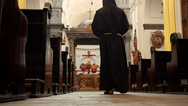Fraile franciscano monje sacerdote caminando en oración meditando rezando hincado ante el altar con Cristo al fondo en templo iglesia parroquia en la casa de Dios