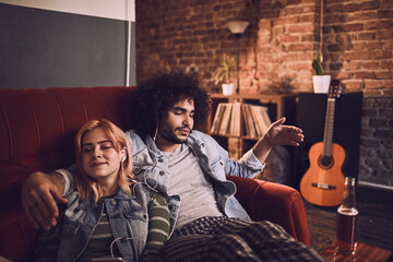 Young and diverse couple listening to music on the headphones together on the couch at home