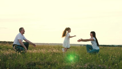 Cute little girl runs from loving mother to father paying in summer field