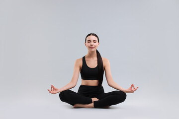 Beautiful young woman practicing yoga on grey background. Lotus pose