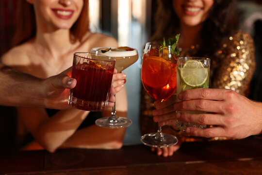 Friends clinking glasses with fresh cocktails in bar, closeup