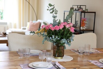 Beautiful table setting with bouquet in dining room. Roses and eucalyptus branches in vase