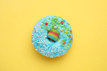 Glazed donut decorated with sprinkles on yellow background, top view. Tasty confectionery