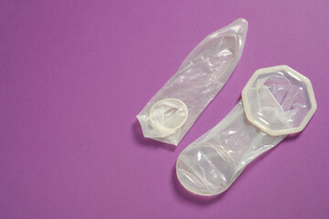 Unrolled female, male condoms on violet background, flat lay with space for text. Safe sex