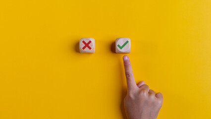 Right and wrong icons on wooden cubes with hand choosing the right icon on yellow background....
