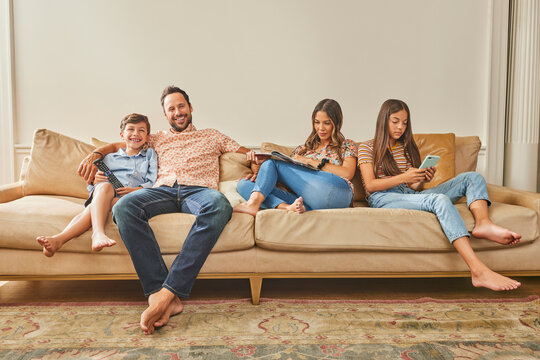 Smiling family with two children (8-9, 12-13) relaxing on sofa