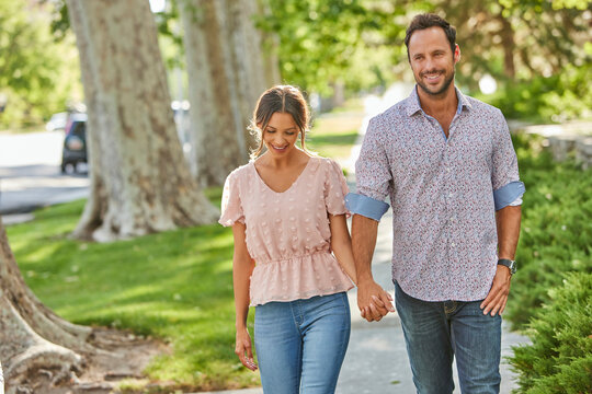 Smiling couple holding hands, walking on treelined sidewalk