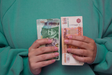 Woman in green long sleeved sweater holds stack of paper money. Russian banknote 5000 rubles and Georgian bill 50 lari in female hand. Cash in Georgia and Russia for tourism, travel, payments, salary