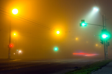 City foggy road intersection at night. Bright traffic lights shining on street lamp on soft copy space bokeh background. Defocused multicolor lights pattern