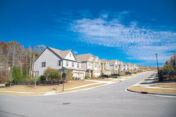 Intersection of large residential streets with row of upscale new development two story suburban houses shingle roofs under sunny blue cloud sky suburbs of Atlanta, Georgia, USA