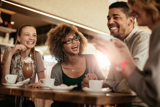 Young and diverse group of friends having a conversation over some coffee and desserts in a cafe