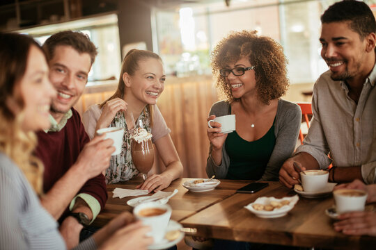 Young and diverse group of friends having a conversation over some coffee and desserts in a cafe