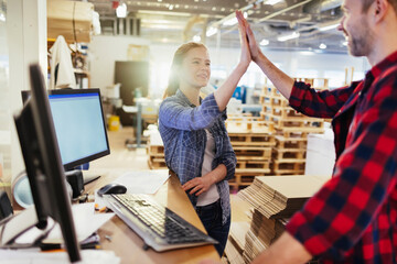 Two Caucasian coworkers congratulating each other while working in a warehouse