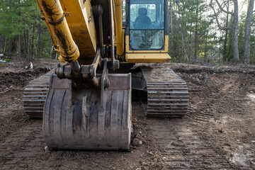 Closeup of the bucket and tracks of an excavator on the soil near trees, in a new home construction...