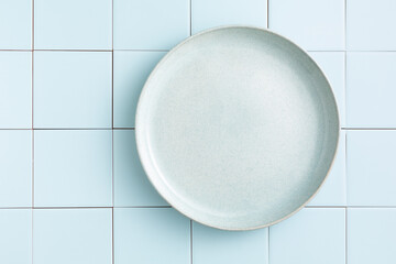 An empty blue plate on a blue tiled background. Copy space, Top view.