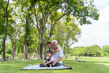 Two Asian granddaughters with grandpa and grandma sitting and talking on the grass outdoors in the park during the day.