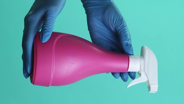 Vertical video. Disinfectant spray. Effective cleaning. Houseworker hands in protective latex gloves demonstrating pink bottle isolated on green background.
