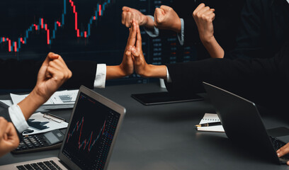 Group of stock trading investors in brokerage firm company celebrating together after achieving profitable gain from selling stocks, expressing joy through celebratory high five gesture. Trailblazing