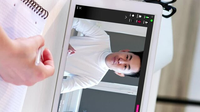 Vertical video. Internet learning. Home education. Online class. Woman student hand writing notes man coach speaking at virtual lesson on tablet screen at workplace.