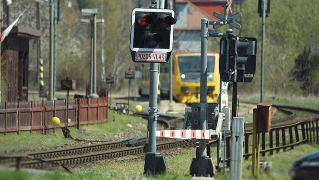 A railway crossing closed with signals flaring as the train is waiting at the station