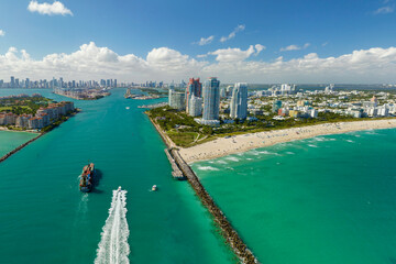Aerial view of container ship entering in Miami harbor main channel near South Beach. Luxurious hotels and apartment buildings on waterfront and high skyscrapers of downtown district in distance